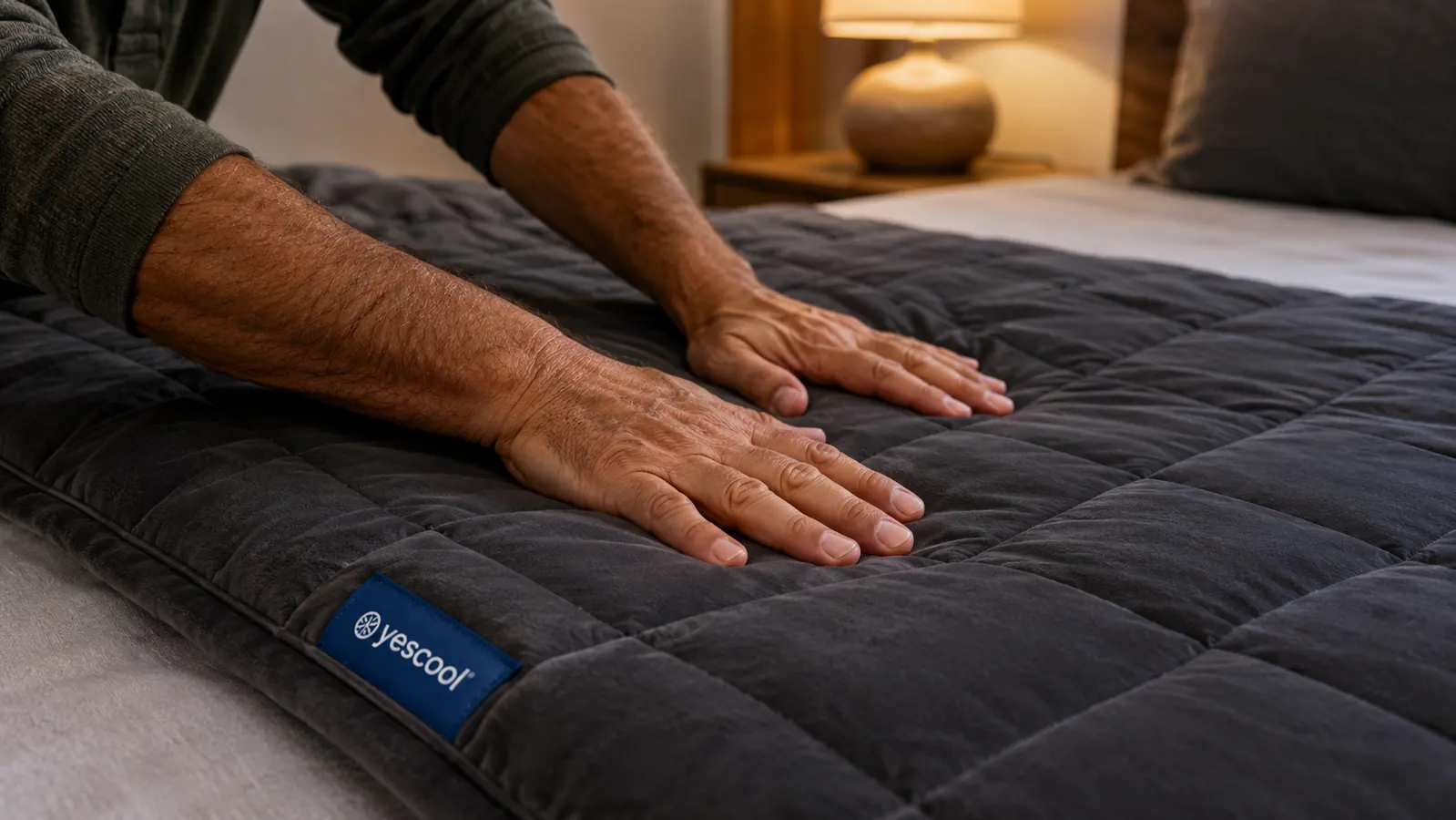 Hands smoothing a purple weighted blanket over a made bed, showing the quilted grid stitching that holds the glass beads in place