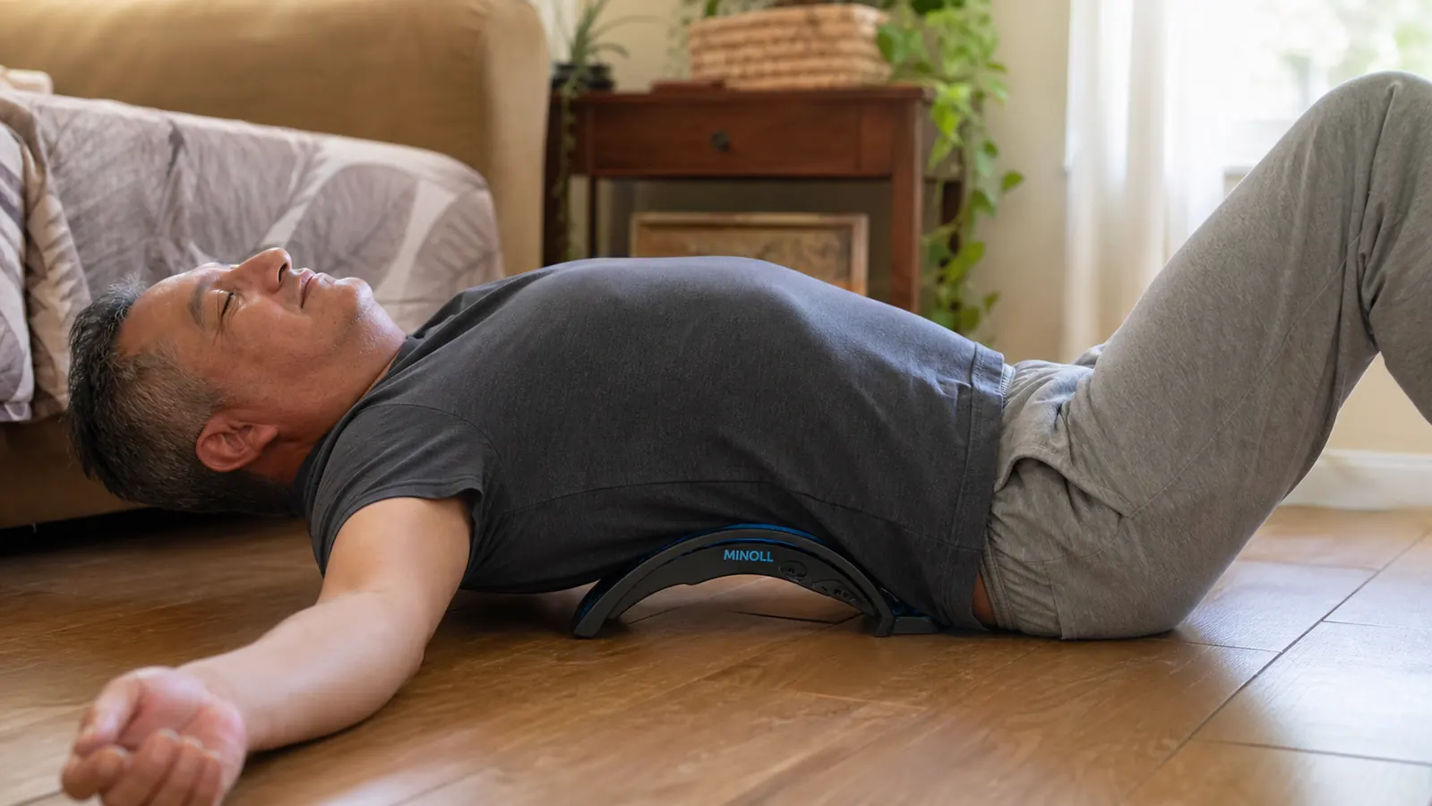 A man lying on his back on a living room floor using a curved plastic back stretcher arch under his lower back
