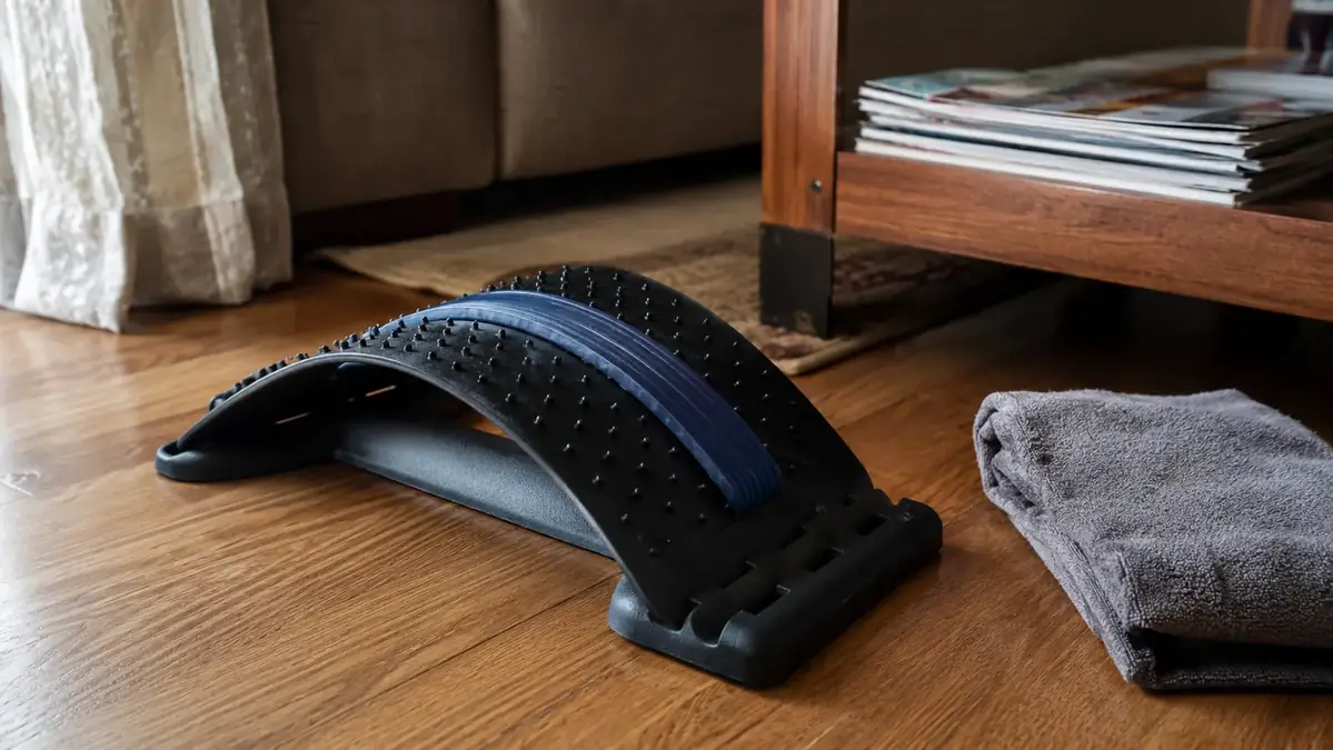A curved plastic back stretcher arch set on a living room floor next to a coffee table, morning light coming through a window